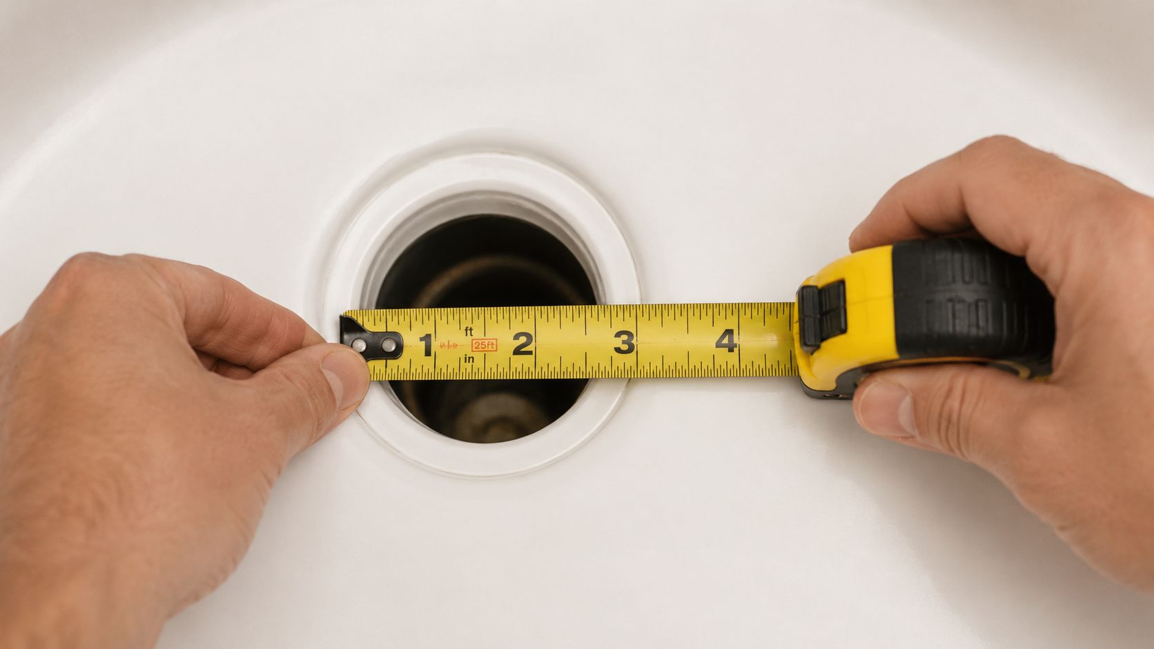 A pair of hands using a measuring tape to measure the diameter of a white shower drain.