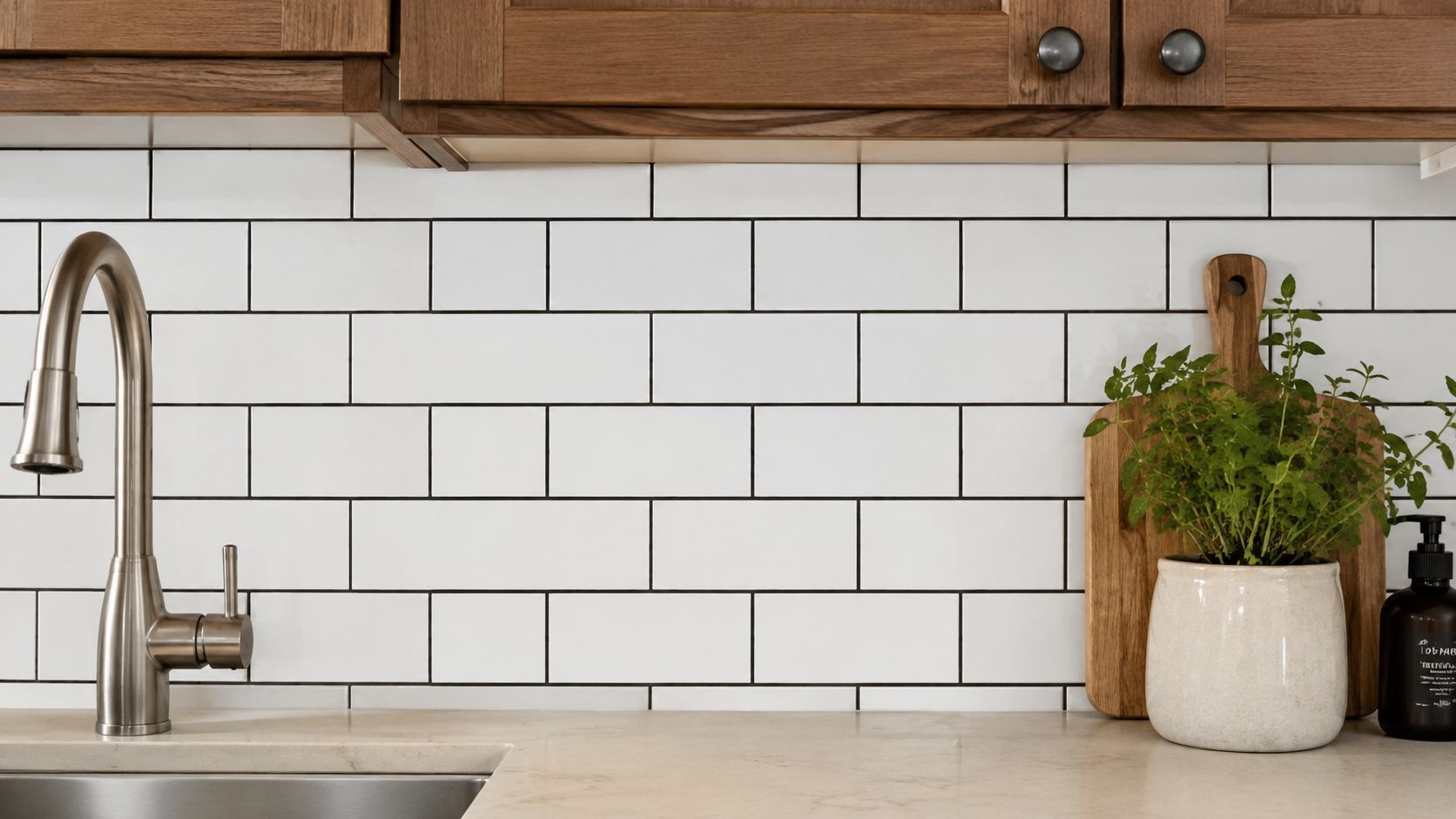 A modern kitchen sink area featuring white subway tile backsplash, wooden cabinets, and a potted plant.