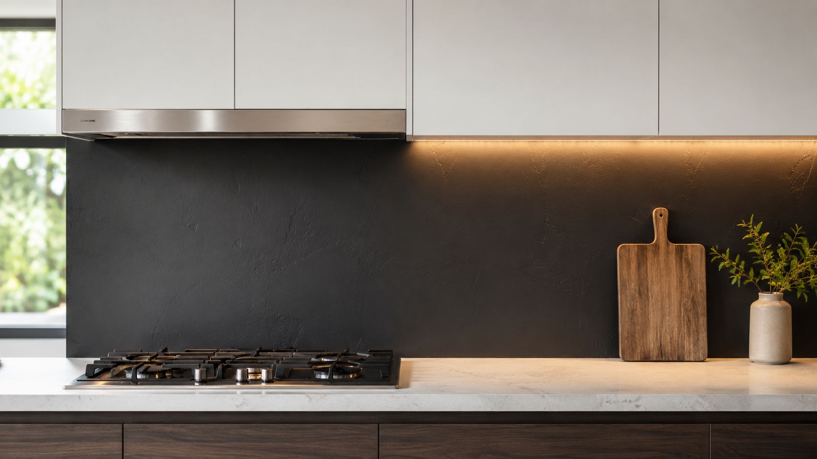 A modern kitchen with a dark charcoal textured backsplash, light marble countertop, and a wooden cutting board.